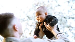 Father, side view, holding baby in sweater in front of his face above eye level